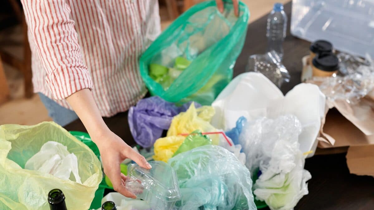 Personne triant des plastiques et bouteilles recyclables en intérieur, après un débarras et avant l'envoi en filière.