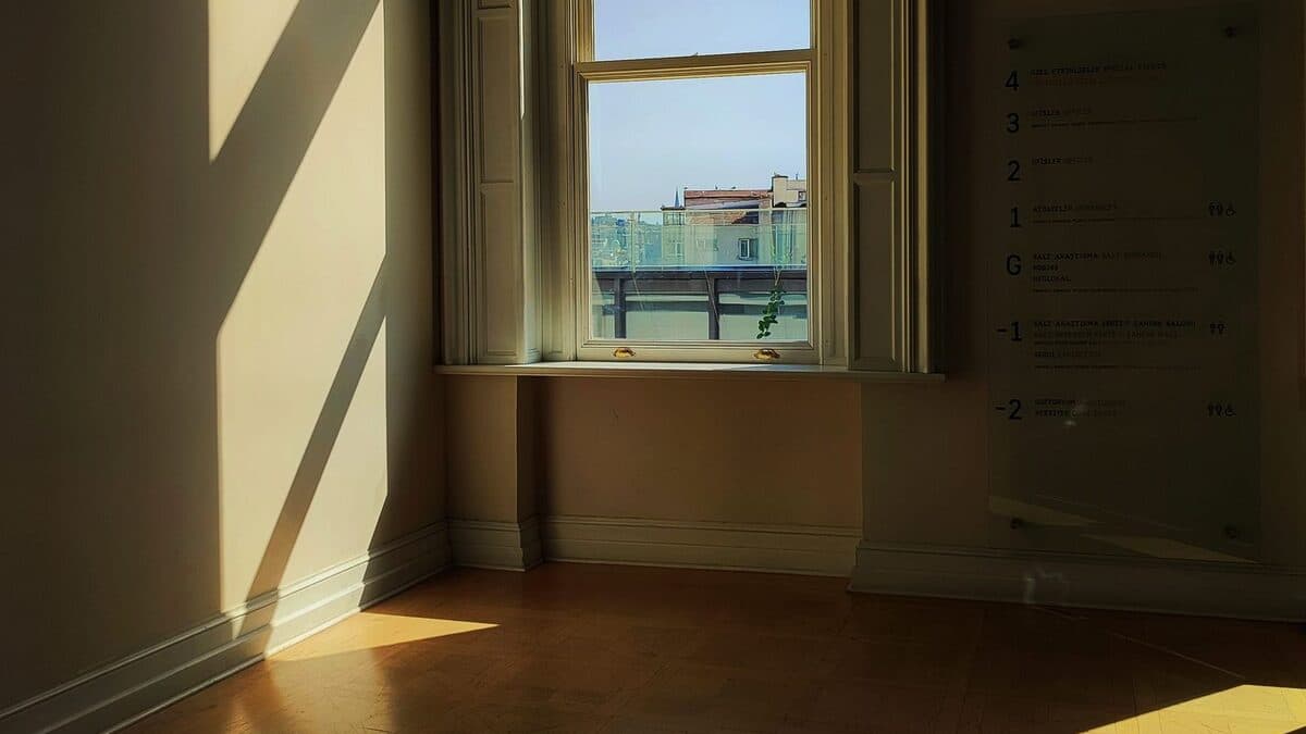 Pièce vide d'une maison après un décès, lumière douce du jour entrant par la fenêtre sur le parquet.